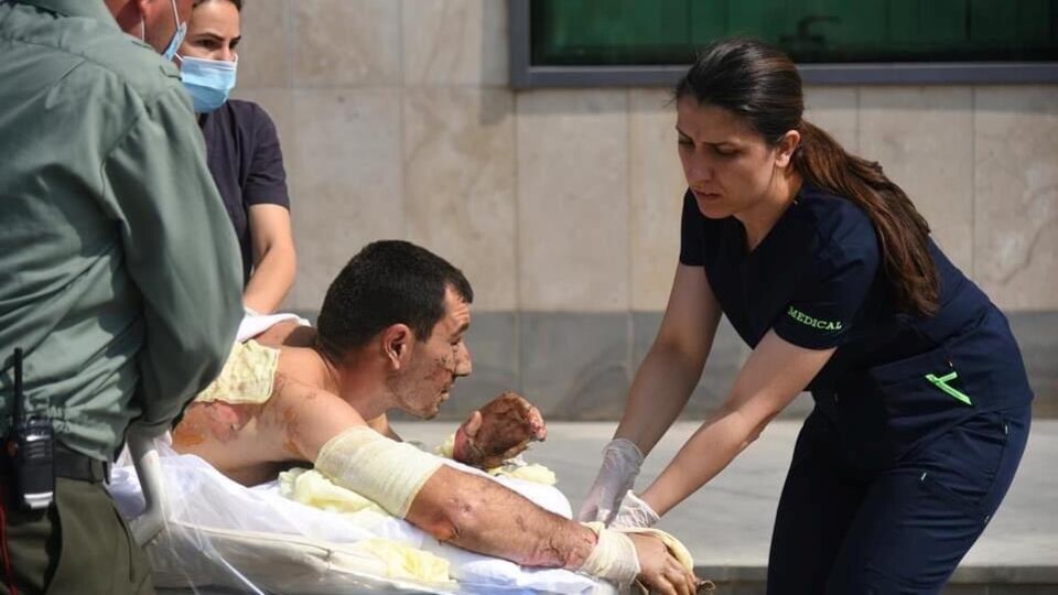 Un homme est allongé sur le ventre sur une civière, son dos et ses bras semblent avoir subi des blessures et du personnel médical le prend en charge à l'extérieur d'un hôpital.
