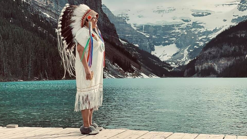 La cheffe contestée de la Première Nation crie Peter Ballantyne, en Saskatchewan, debout sur un quai, devant un lac et des montagnes enneigées. 