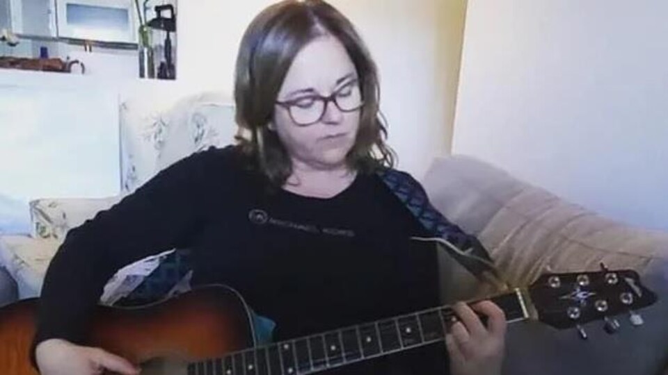 Une femme joue de la guitare, assise sur un canapé.