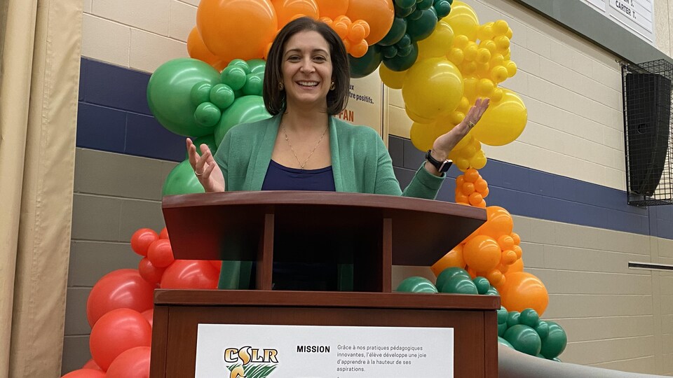 Karine Pilotte debout derrière un lutrin dans une salle décorée de ballons colorés.