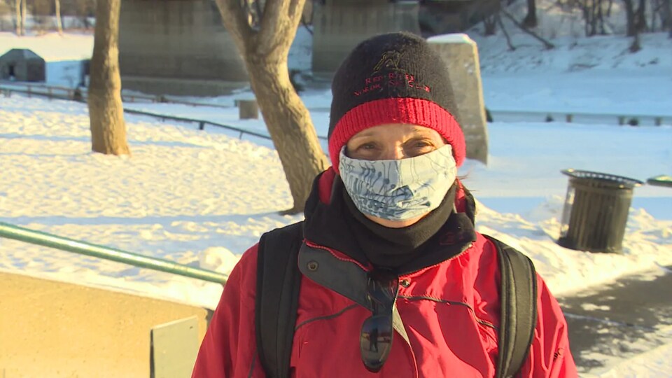 Kate Okany est dehors au soleil, portant une tuque, un manteau et un masque.