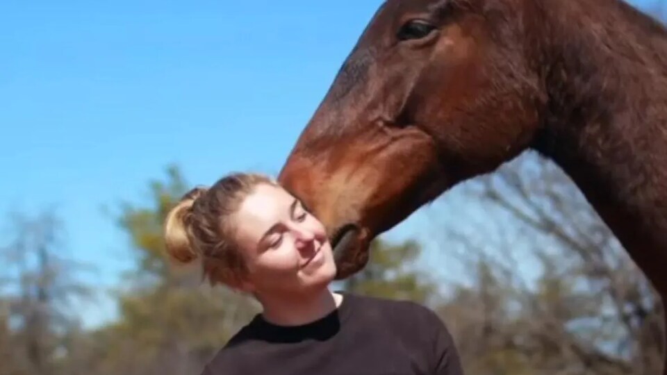 Une jeune femme sourit à côté d'un cheval.