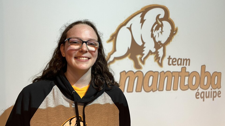 Kaylee Perry devant le logo de l'équipe Manitoba.