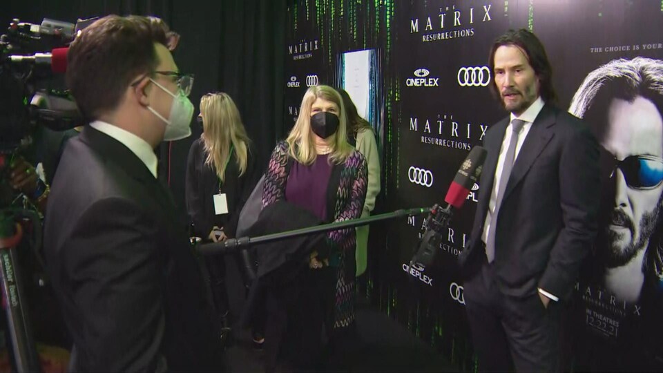 L'acteur répond aux question d'un journaliste avec une perche devant l'affiche du dernier film de la saga « La Matrice ».