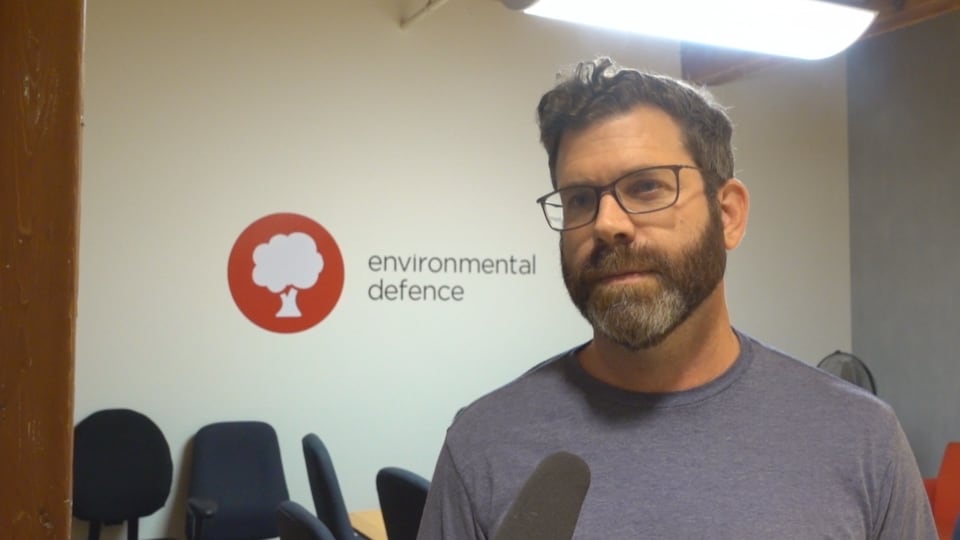 Un homme dans une salle avec un mur où l'on peut lire « environmental defence». 
