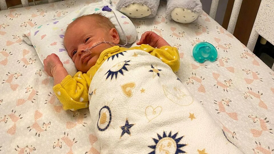 Un bébé dans un lit de bébé à l'hôpital. Une peluche et une suce sont déposées à côté de lui.