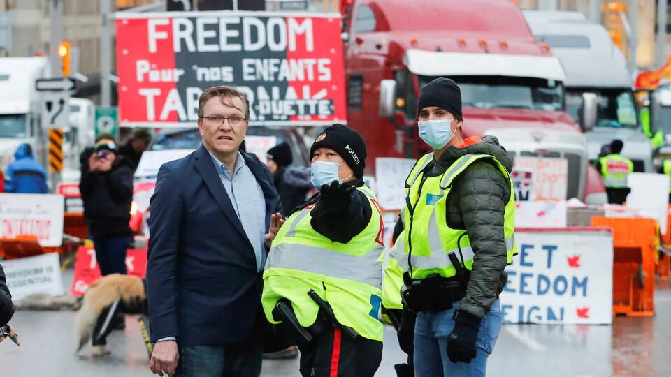 Keith Wilson discutant avec un policier devant des camions stationnés lors d'une manifestation.