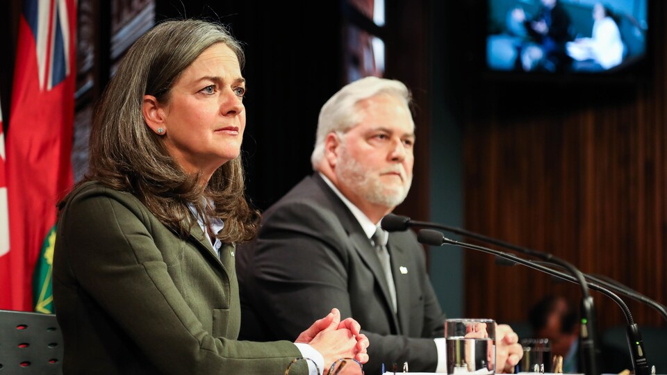 Une femme et un homme en arrière-plan à ses côtés dans une salle de presse de l'édifice de l'Assemblée législative de l'Ontario.