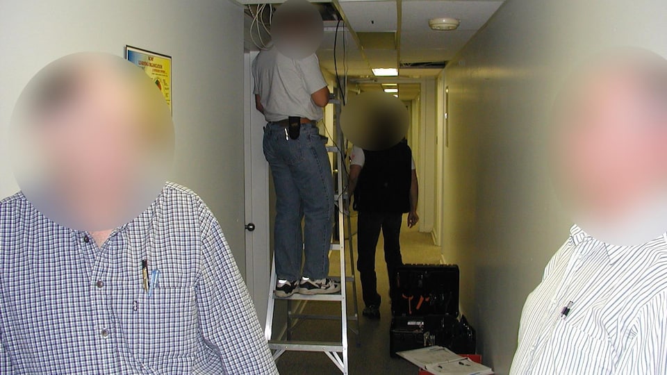 Des personnes dont le visage est brouillé sont dans un couloir. L'un d'entre eux est sur un escabeau et tient des câbles sortant du plafond.