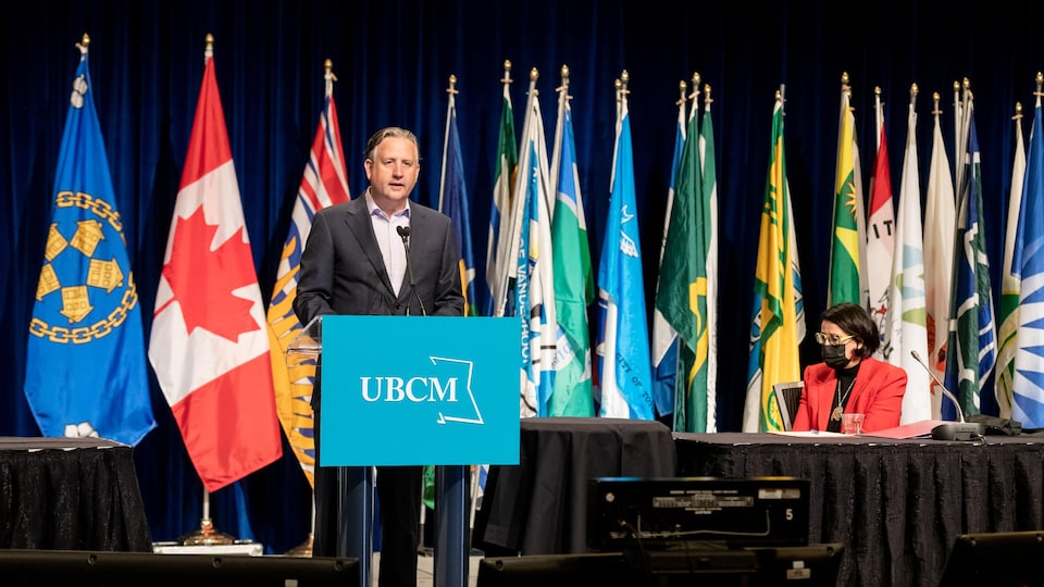 Kennedy Stewart, maire de Vancouver, à un pupitre du Congrès de l'Union des municipalités de la Colombie-Britannique, devant de multiples drapeaux.