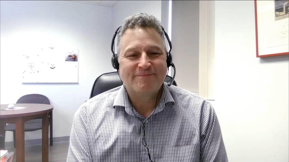 Kenneth Deveau assis devant son ordinateur, avec des écouteurs, filmé par sa webcam.