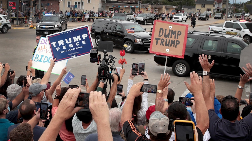 Tandis que le convoi présidentiel circule sur la rue, des dizaines de personnes se tiennent près du chemin, pancartes à la main.