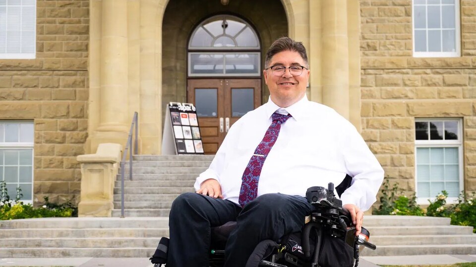 L'ancien député Kent Hehr est assis sur un fauteuil roulant devant les escaliers d'un bâtiment.