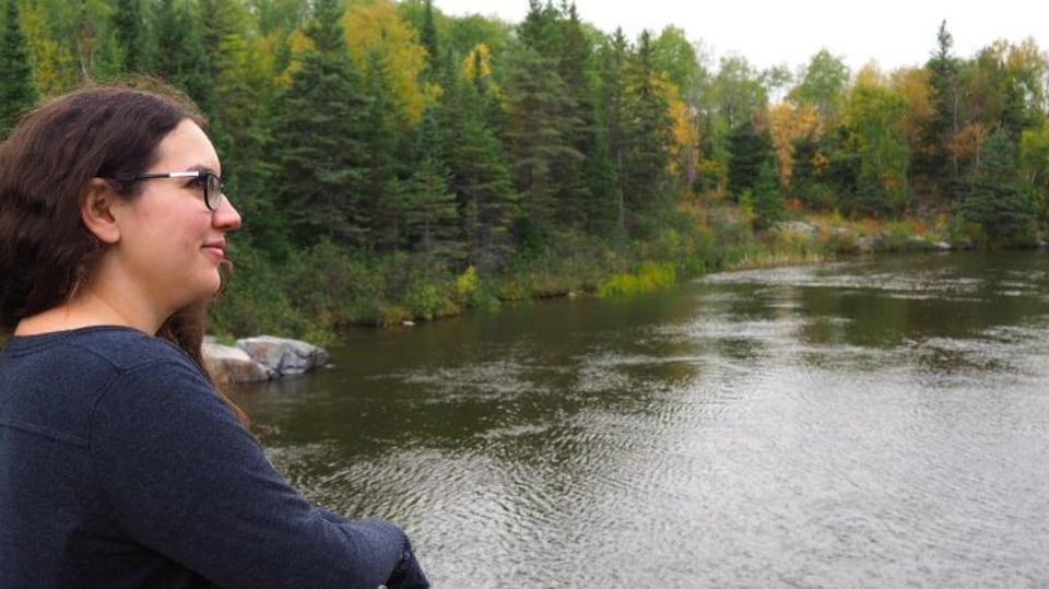 Une femme sur un pont suspendu au-dessus une rivière en pleine forêt regarde vers l'horizon.