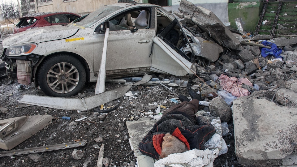 Le corps d'un homme gît dans des décombres près d'une voiture.