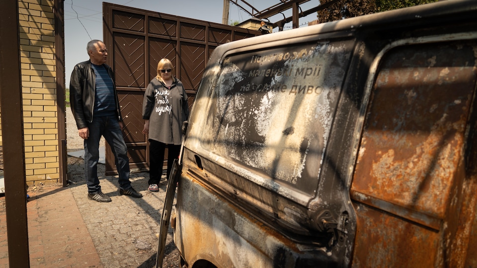 Oleksandr and Lyudmila behind a charred van.