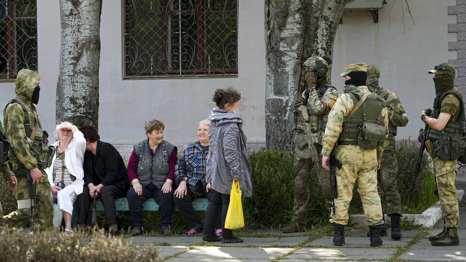 Des aînés sur un banc entourés de militaires russes non-identifiables.