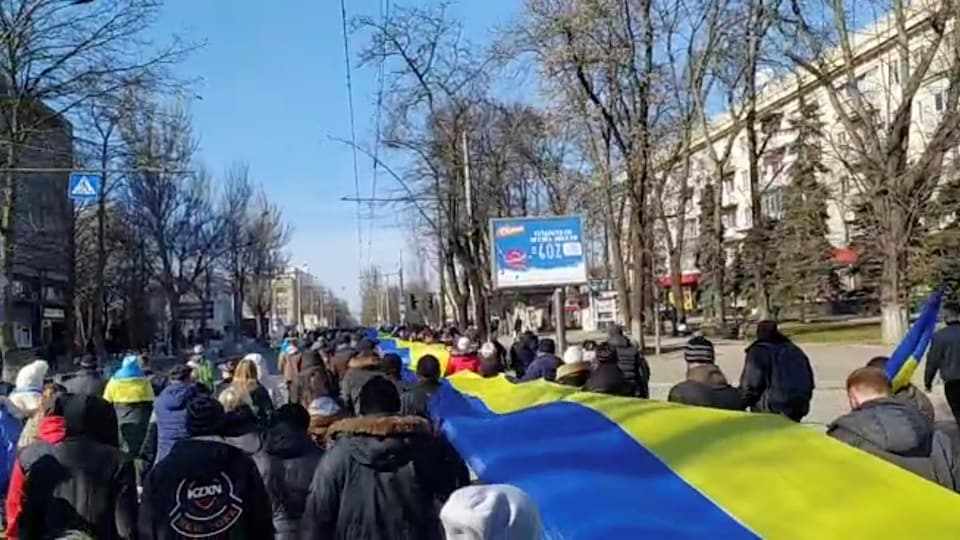 Des gens marchent dans une rue en tenant une longue banderole aux couleurs du drapeau ukrainien.