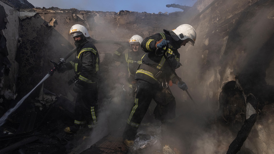Trois pompiers au travail dans les décombres fumants d'une maison détruite. 
