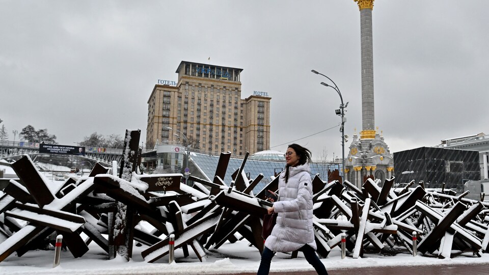 Une femme marche près d'équipement militaire recouvert de neige.