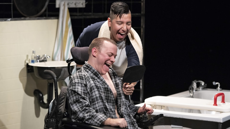 Deux hommes rient en se regardant dans un miroir à main. L'un est debout et l'autre en fauteuil roulant.