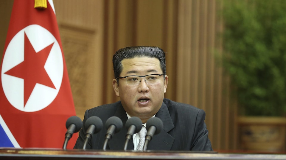 Kim Jong-un parle dans cinq micros, devant un drapeau nord-coréen.