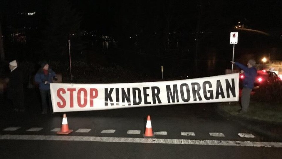 Deux hommes tiennent une banderole où il est écrit, Stop Kinder Morgan.