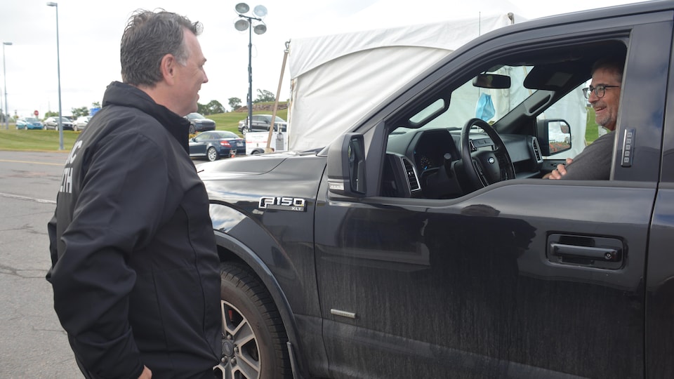 Dennis King debout parle à un homme souriant au volant d'une camionnette.