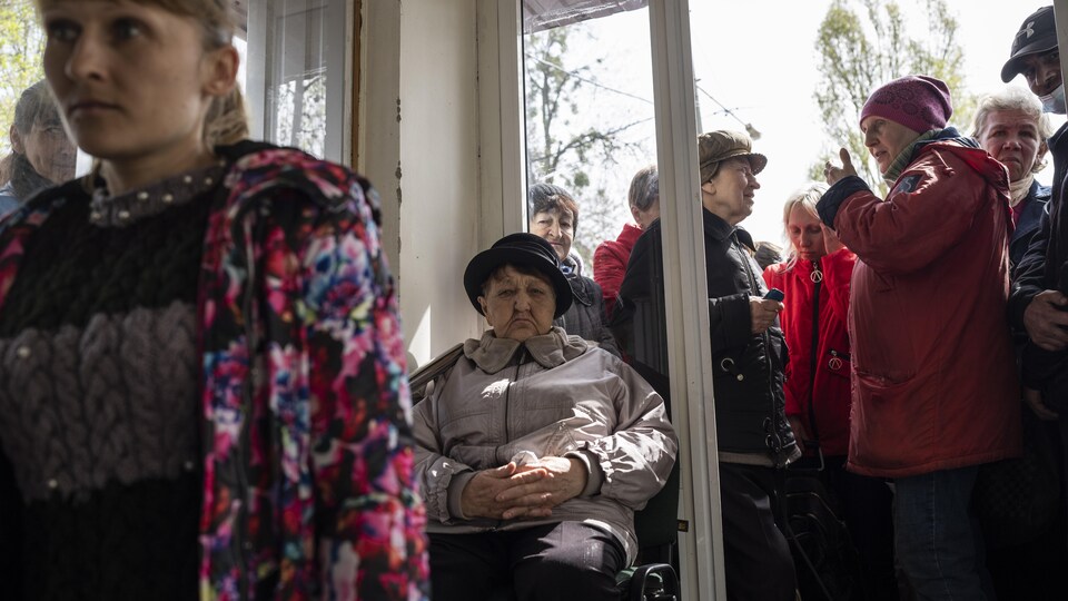 Des femmes et des personnes âgées attendent à l'intérieur et à l'extérieur d'un immeuble. Une femme est assise dans un fauteuil roulant.