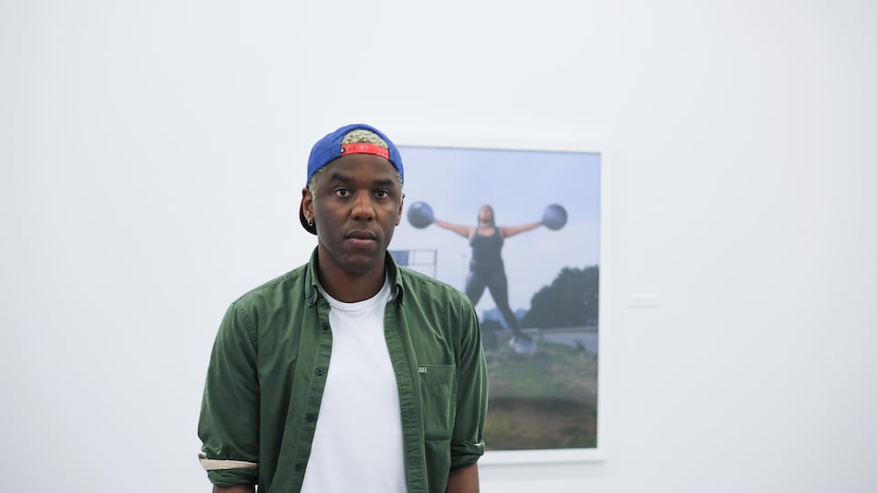 L'artiste Kriss Munsya devant une de ses photos dans une salle d'exposition.