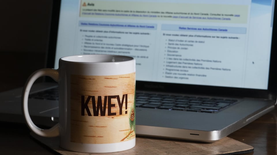 Une tasse sur laquelle il est écrit kwey, devant un écran d'ordinateur portable.
