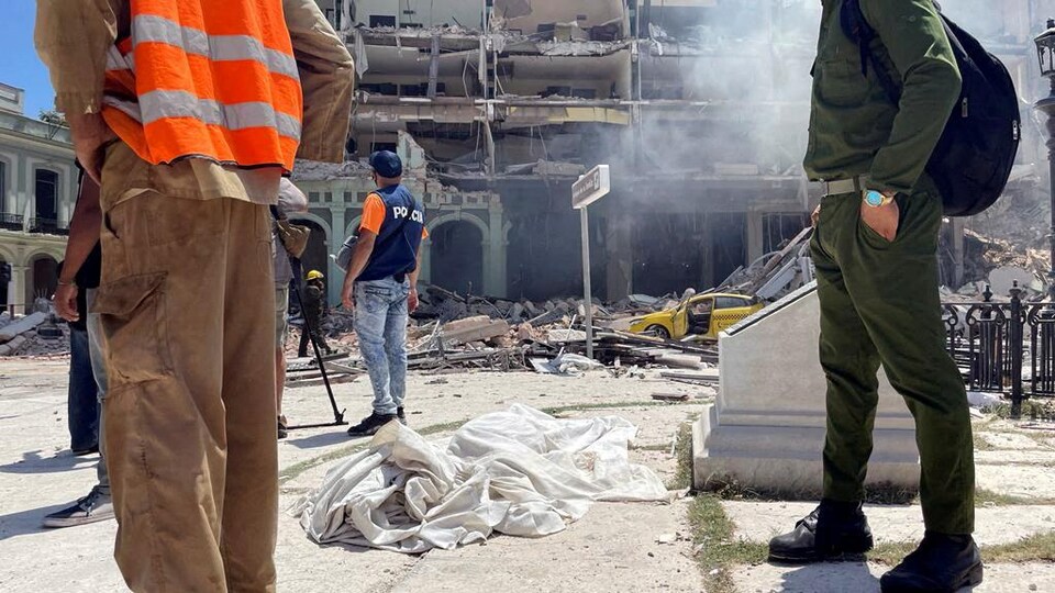 Des secours se trouvent devant un hôtel en ruines, près du corps d'une victime sous un drap.