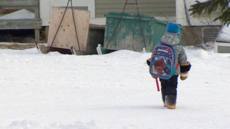 Un enfant marche dans la neige avec son sac d'école.