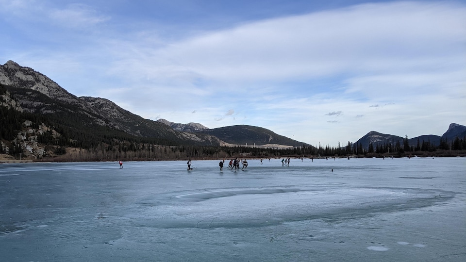 Des patineurs sur un lac gelé au milieu des montagnes.