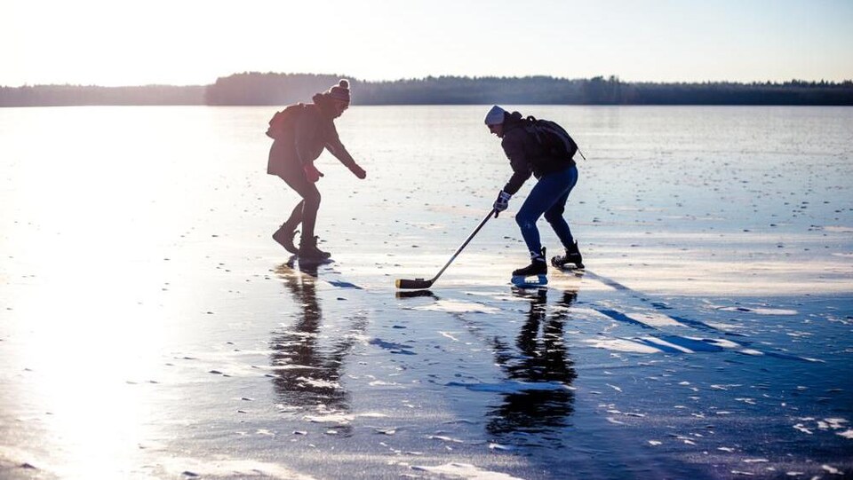 Deux personnes jouent au hockey sur un immense lac gelé.
