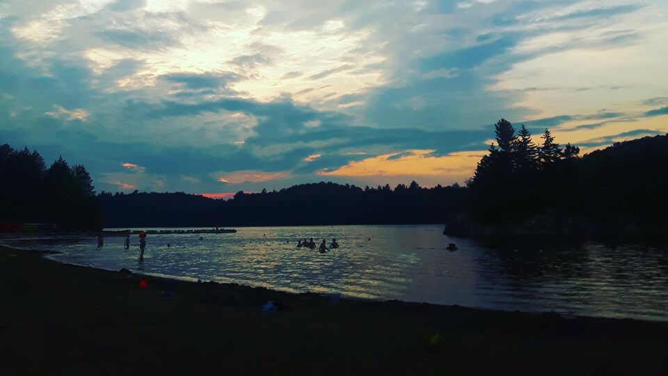 La plage du lac Stukely a été fermée temporairement après des tests effectués le 3 juillet. Des baigneurs se baignent au coucher du soleil.
