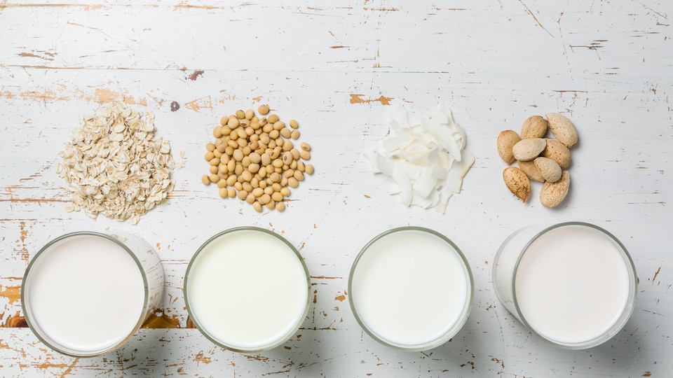 Des noix sont posées devant des verres de lait sur une table, comme pour signifier que ces verres de lait sont en fait des boissons à base de soja, d'amandes ou d'avoine.