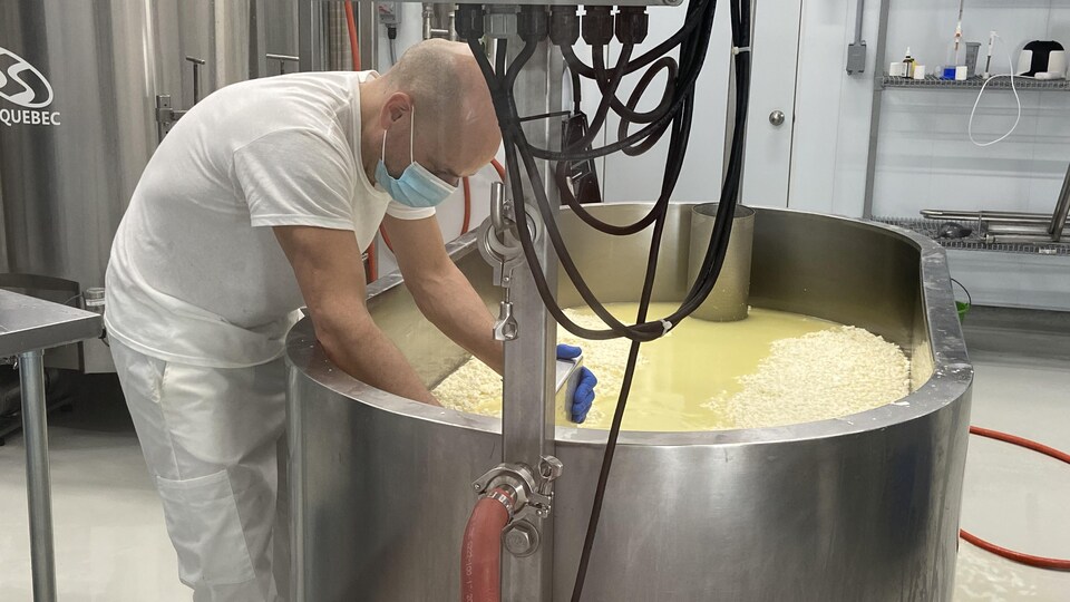 Une cuve de métal dans laquelle est produit du fromage. Un employé se trouve devant la cuve.