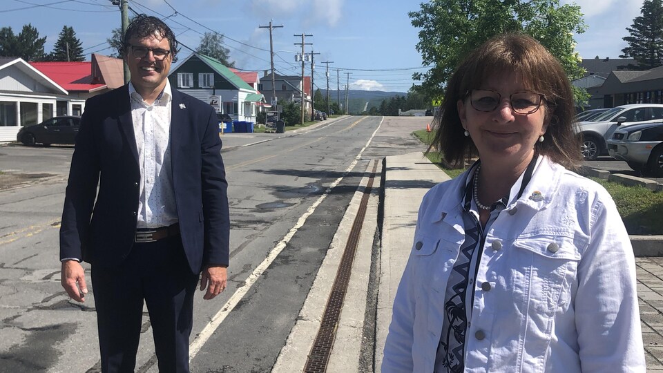 Un homme et une femme sourient devant une route en mauvais état.