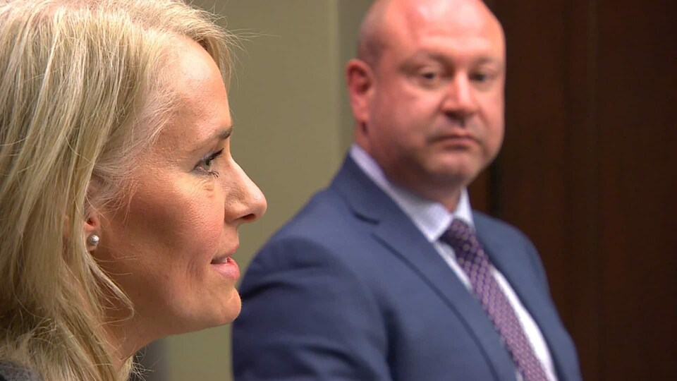 Lanette Siragusa parle, à l'avant-plan et vue de profil, et en arrière-plan, Brent Roussin, vu de face, la regarde.
