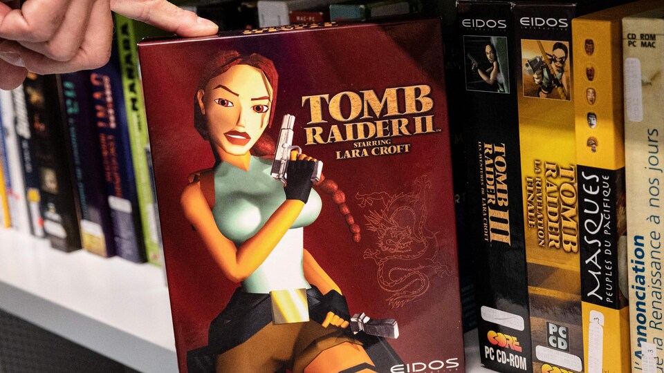Une copie du jeu tomb raider, retirée par une main d'un rayon à partir d'une tablette remplie d'autres jeux vidéo. 