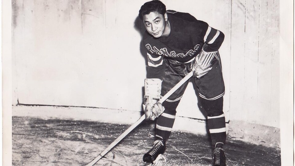 Larry Kwong sur la glace tenant un bâton de hockey. 