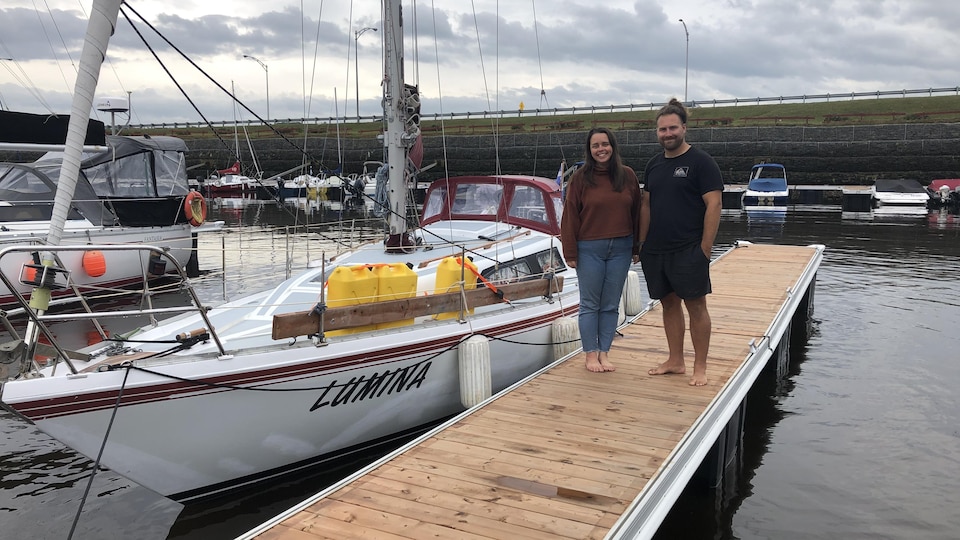 Un couple pose devant un voilier dans une marina.