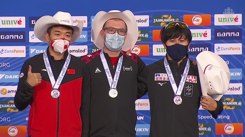 Trois hommes côte à côte portant un masque, un chapeau de cow-boy et une médaille autour du cou.