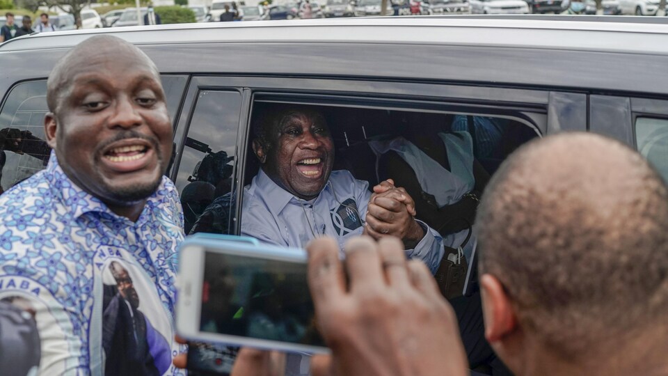 Une foule encercle une voiture dans laquelle se trouve l'ex-président, souriant.
