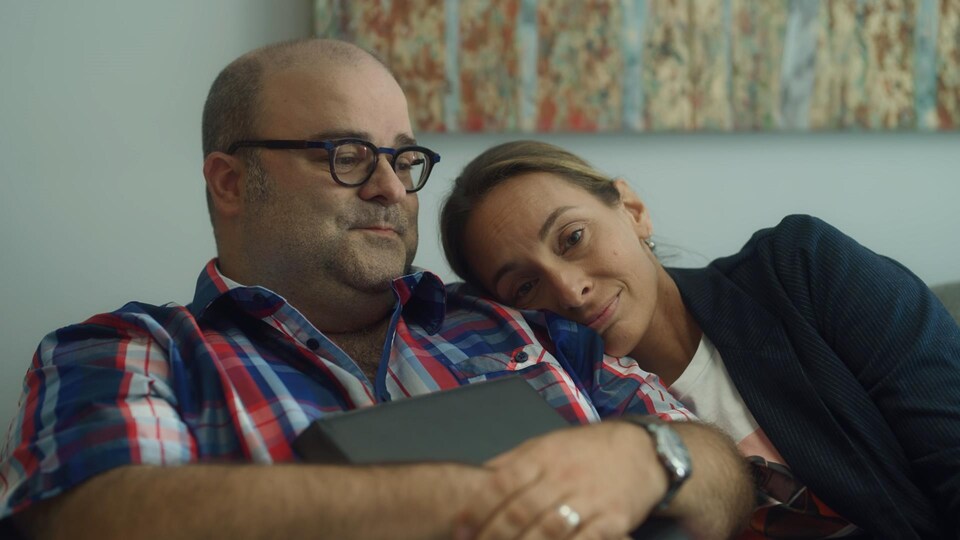 L'homme et la femme sont sur un divan et la femme met sa tête sur l'épaule de l'homme.