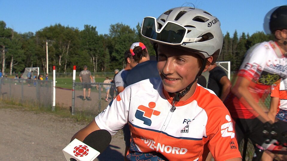 Laurent Pelletier se tient sur son vélo de montagne lors de l'entrevue. Il porte un maillot orange, un casque et des lunettes de vélo.