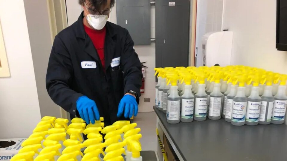 Un homme avec des gants et un masque manipule des bouteilles de désinfectant.