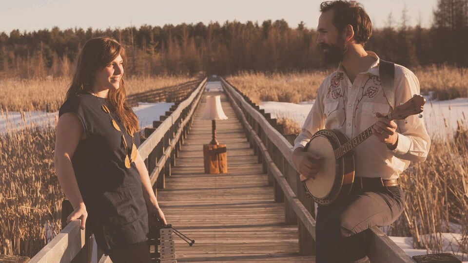 Photo prise à l'automne en plein-air qui nous montre Kaitlin Milroy et Alex Millaire au banjo sur un pont piétonnier