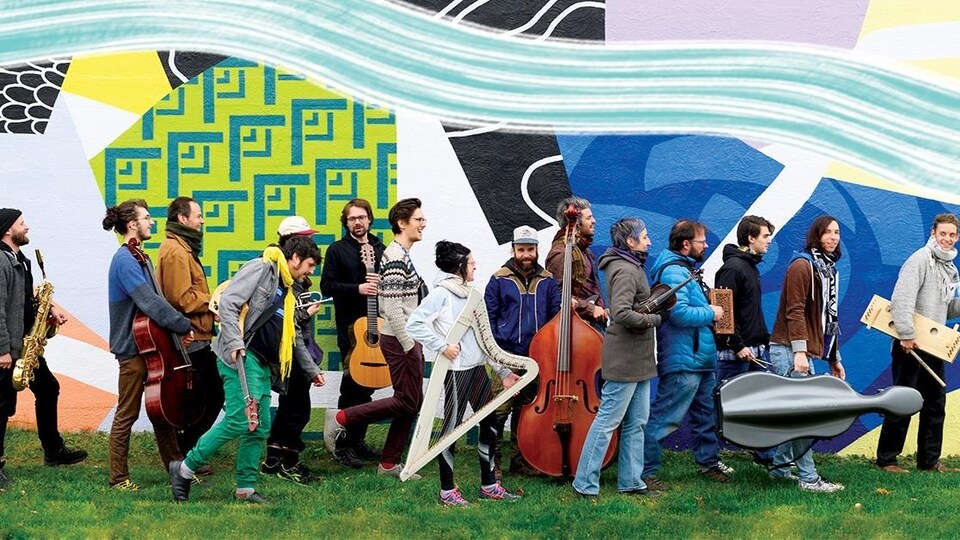 Quinze membres du GGRIL, le Grand groupe régional d'improvisation libérée, à Rimouski devant la murale de colorée du Centre d'artistes Caravansérail.
